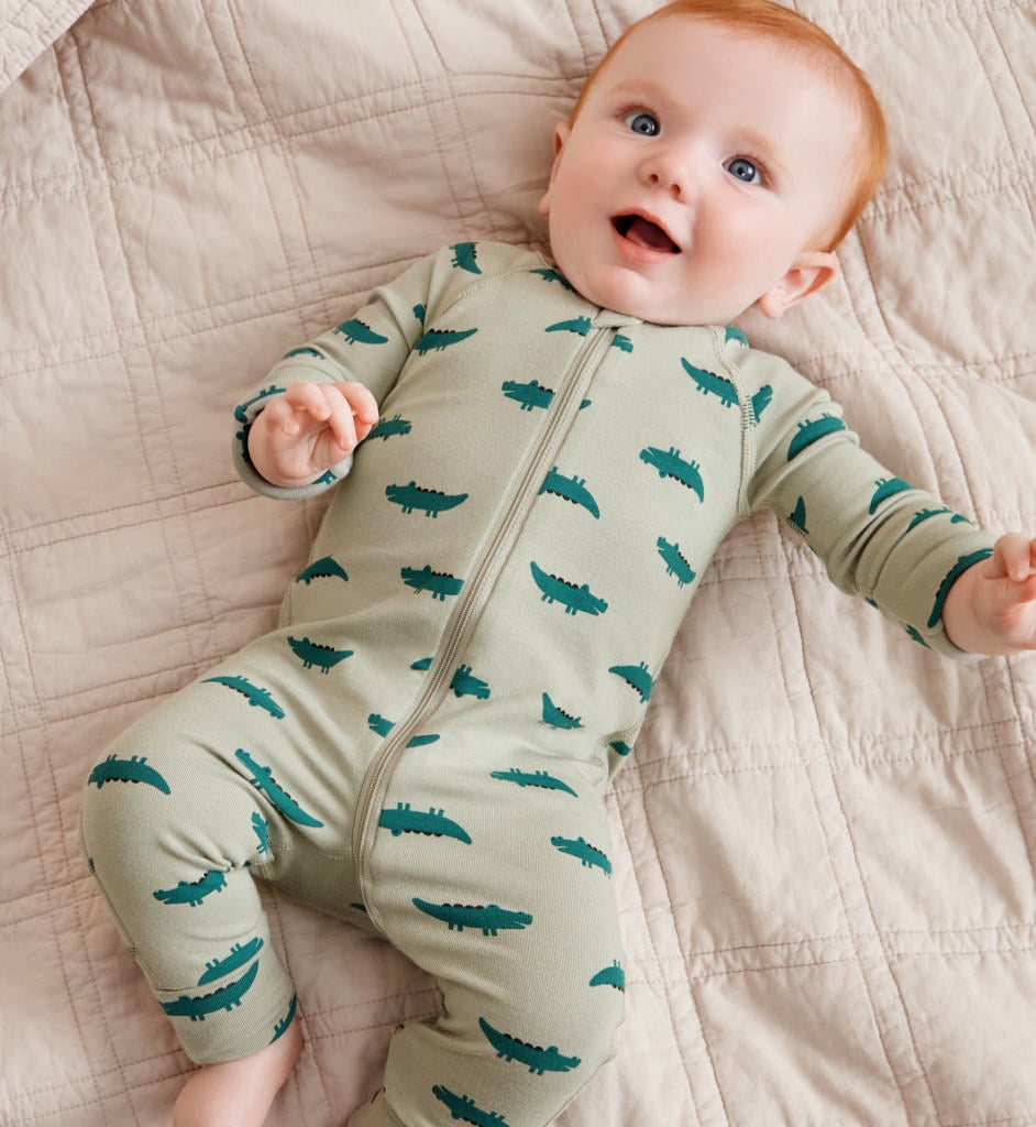baby lying down wearing a green baby sleeper