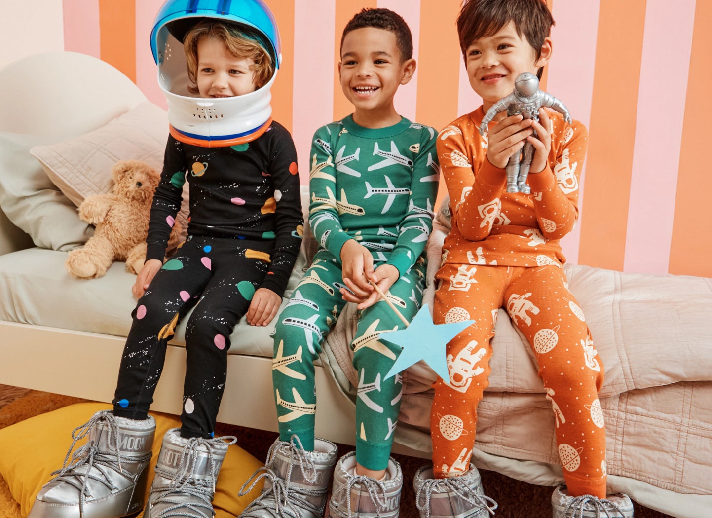 Three children in patterned pajamas sitting on a bed