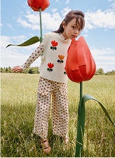 A child in a flower-pattern shirt smelling a large tulip in a field