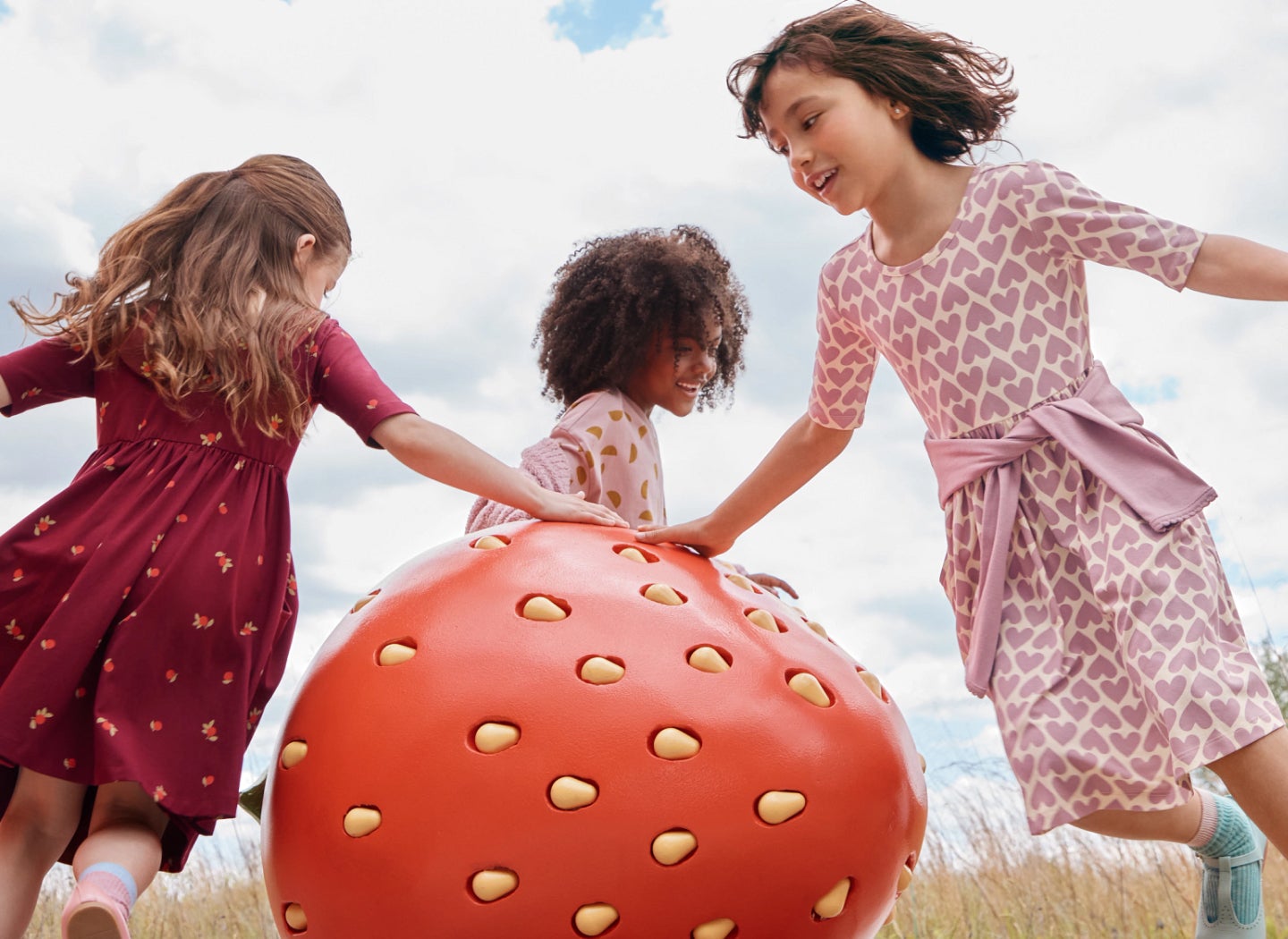 Three girls in dresses dancing around a large strawberry