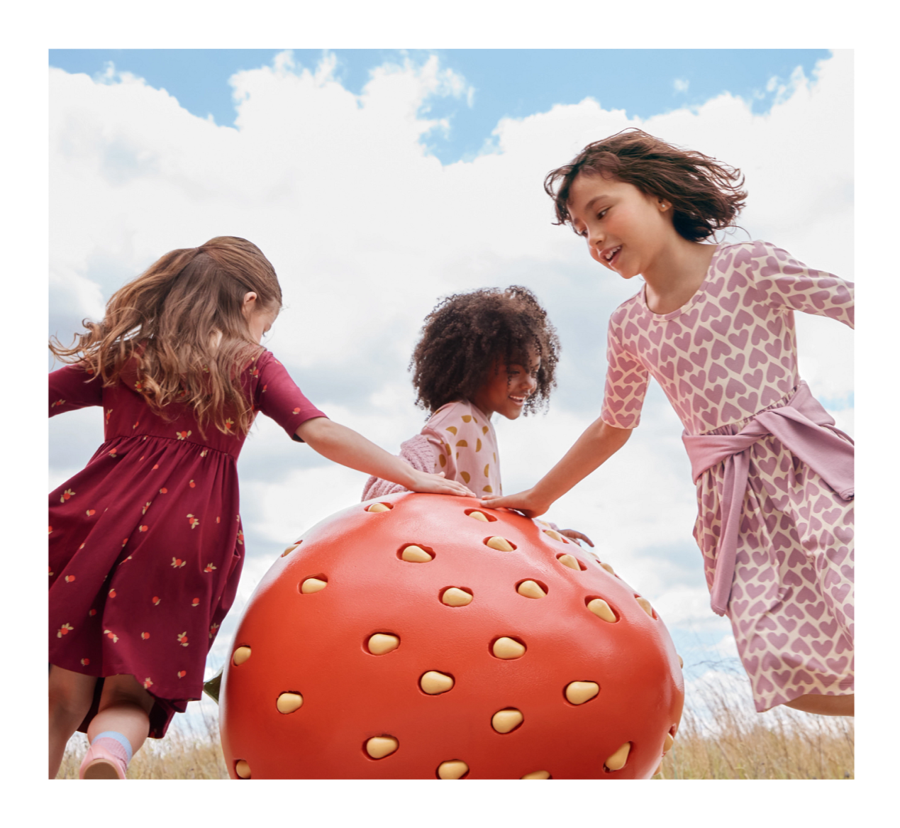 Three girls in dresses dancing around a giant strawberry